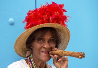 Old Cuban woman smokes a Cuban cigar on the street and posts with her cat for the tourists, La