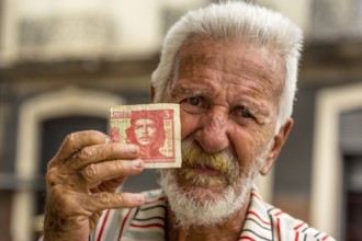 Old Cuban man holding a three peso banknote with the portrait of Ernesto Che Guevara in his hand,