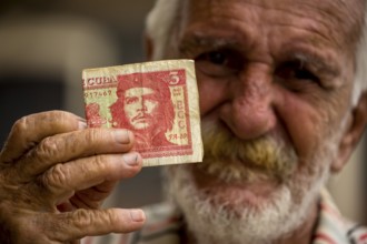 Old Cuban man holding a three peso banknote with the portrait of Ernesto Che Guevara in his hand,