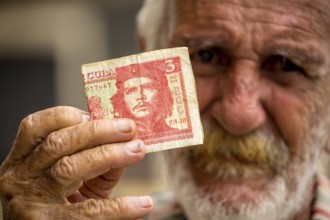 Old Cuban man holding a three peso banknote with the portrait of Ernesto Che Guevara in his hand,