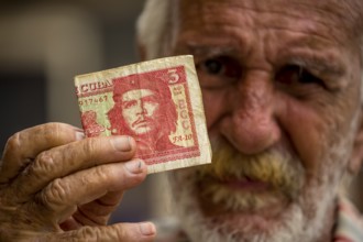Old Cuban man holding a three peso banknote with the portrait of Ernesto Che Guevara in his hand,
