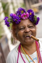 Old Cuban woman with flowers and cigar posing for a tip for tourists, La Habana, Havana, Cuba,