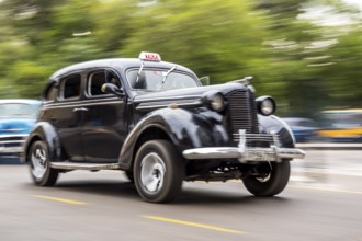 Speed, blurred, moving old car, black oldtimer in street scene, old american street cruiser on the