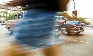 Part of a pedestrian in front of cars, speed, blurred, moving old car, vintage car in street scene,