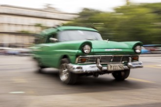 Speed, blurred, moving old car, green oldtimer in street scene, old american street cruiser on the