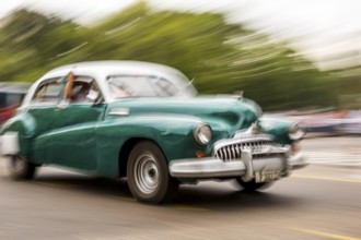 Speed, blurred, moving old car, green oldtimer in street scene, old american street cruiser on the