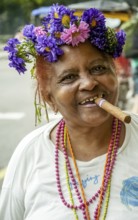 Old Cuban woman with flowers in her hair smoking a cigar and post for the photographer, La Habana,