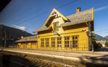 Yellow wooden railway station building Vaksdal, railway tracks, blue sky, near Bergen city railway