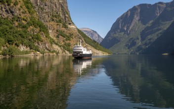 An approaching excursion boat on a beautiful fjord reflecting the light, surrounded by rocks partly
