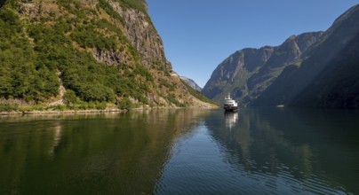 An approaching excursion boat on a beautiful fjord reflecting the light, surrounded by rocks partly