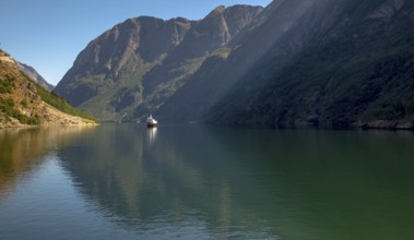 An approaching excursion boat on a beautiful fjord reflecting the light, surrounded by rocks partly