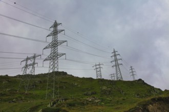 Electricity pylons on an overgrown hill under a cloudy sky, embedded in a natural landscape, power