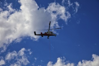Small helicopter in the blue sky with few clouds, transport helicopter, timber transport, Saas