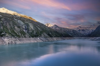 Early morning light over a lake with snow-covered mountains and pink sky, Mattmark reservoir, Saas