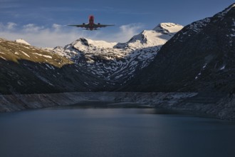 Aeroplane flying over a mountain lake with snow-covered peaks under a blue sky, Mattmark reservoir,