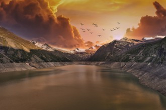 Dramatic sunset over a mountain lake with flying birds and clouds, Mattmark Reservoir, Saas