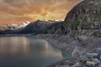 Sunset over a mountain lake with snowy peaks and rocky cliffs, Mattmark reservoir, Saas Almagell,