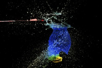 A blue water balloon bursts bubbling, with an arrow and yellow elements in a haunting scene, high