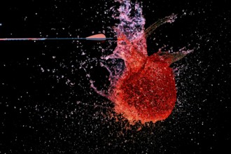 A red water balloon is penetrated by an arrow and creates a lively, powerful water scene,