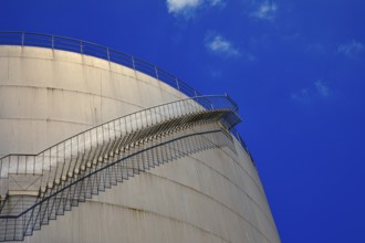 A staircase runs along a large tank in front of a deep blue sky, elevated tank, chemical, company,
