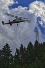 A helicopter flies over a forest and transports a load next to power lines, transport helicopter,