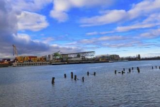 Industrial harbour with containers and cranes under a cloudy blue sky on a river, Rhine, Birsfelden