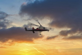 A helicopter flies in front of a dramatic sky with clouds and sunset, transport helicopter, timber