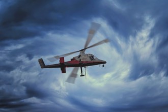 A helicopter flies through a dramatic, stormy blue sky, transport helicopter, timber transport,