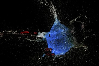 A blue water balloon bursts with force while an arrow shoots through it, surrounded by a dark
