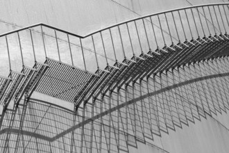 An abstract view of a metal staircase in black and white, emphasised by strong shadow lines,