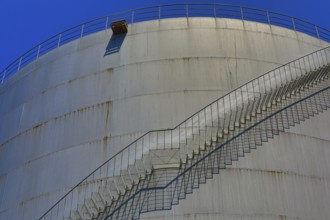 A long metal staircase extends over a large industrial building, illuminated by a clear blue sky,