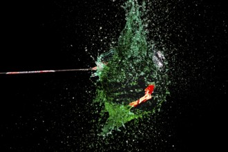 A green water balloon explodes under the impact of an arrow against a dark background, high-speed
