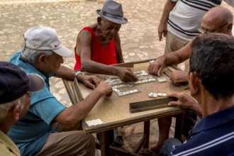 Old Cubans playing dominoes at a table on the street in the city centre of Trinidad, Trinidad,