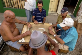 Old Cubans playing dominoes at a table on the street in the city centre of Trinidad, Trinidad,