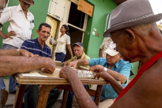 Old Cubans playing dominoes at a table on the street in the city centre of Trinidad, Trinidad,