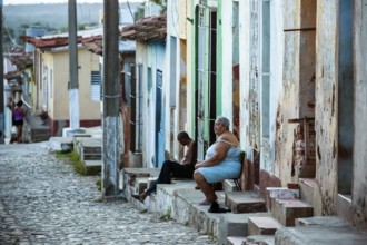 Cubans sitting on their steps in front of their houses in the old town, Street scene in the old