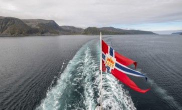 The post symbol on a Norwegian flag of a Hurtigruten ship, foaming spray, Honningsvåg, Finnmark,