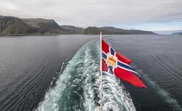 The post symbol on a Norwegian flag of a Hurtigruten ship, foaming spray, Honningsvåg, Finnmark,