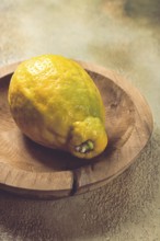 A vibrant lemon sits on a rustic wooden plate, showcasing its uneven texture and vivid color. The