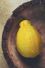 A vibrant yellow lemon sits alone in a wooden bowl with a rough rim, highlighting its natural