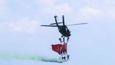 Türkiye special operations police hang from a helicopter with ropes, carrying weapons and unfurling