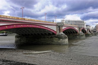 A pink bridge stretches across the Thames, with dense cloud cover above, London, England, United