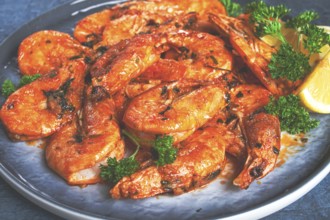 Fried white-footed shrimp, tiger prawns in a bowl, with lemon and herbs, on a blue background