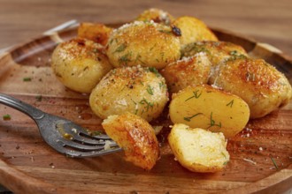 Half-eaten fried new potatoes, with butter and dill, on a wooden plate, with a fork, at home,