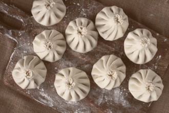 Freshly frozen khinkali, raw, on a wooden chopping board, top view, rustic style, no people