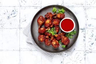 Crispy pieces of fried chicken, on a plate with sauce and herbs, in a modern kitchen environment,