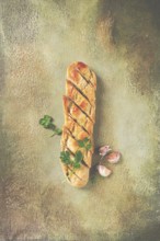 Garlic bread, baguette with garlic butter and herbs, with herbs and garlic cloves