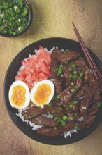 Udon Japanese beef with rice, pickled ginger, boiled egg slice, garnished with green onions, in a