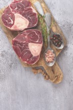 Freshly sliced beef legs, two ossobuco steaks, on a wooden board, with spices and herbs, ready to