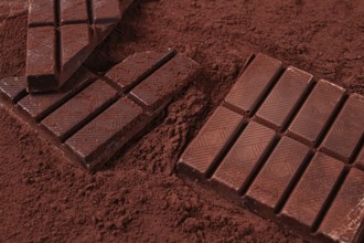 Chocolate bars broken and scattered on cocoa powder background with rich texture and color